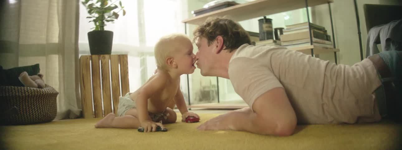 A father and infant son kiss and play together on the carpet of their home