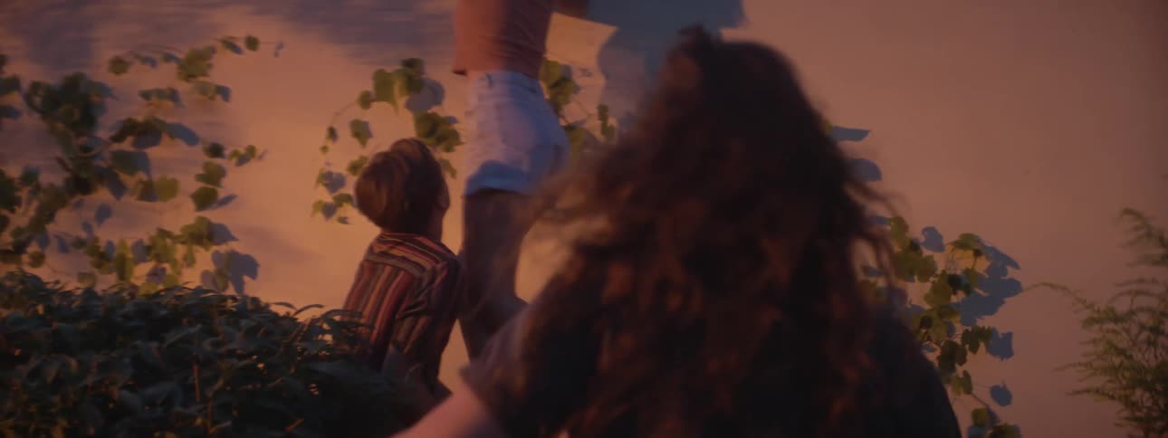 A white teenage girl acts as a lookout for two of her friends starting to climb a high wall