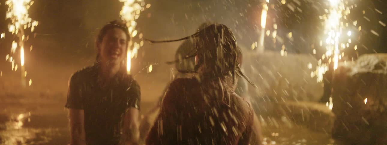 Three teenagers splash around in a lake at night while fireworks shoot off in the background