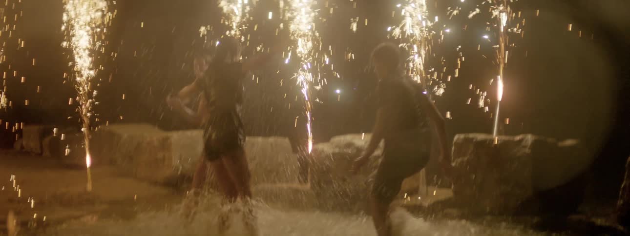 Group of friends play on the beach at night surrounded by fireworks