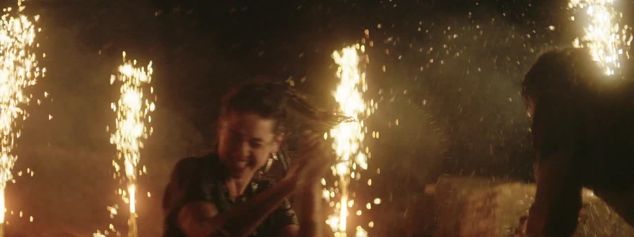 A pair of young women and a young man splashing each other with water in a shallow pool surrounded by fireworks