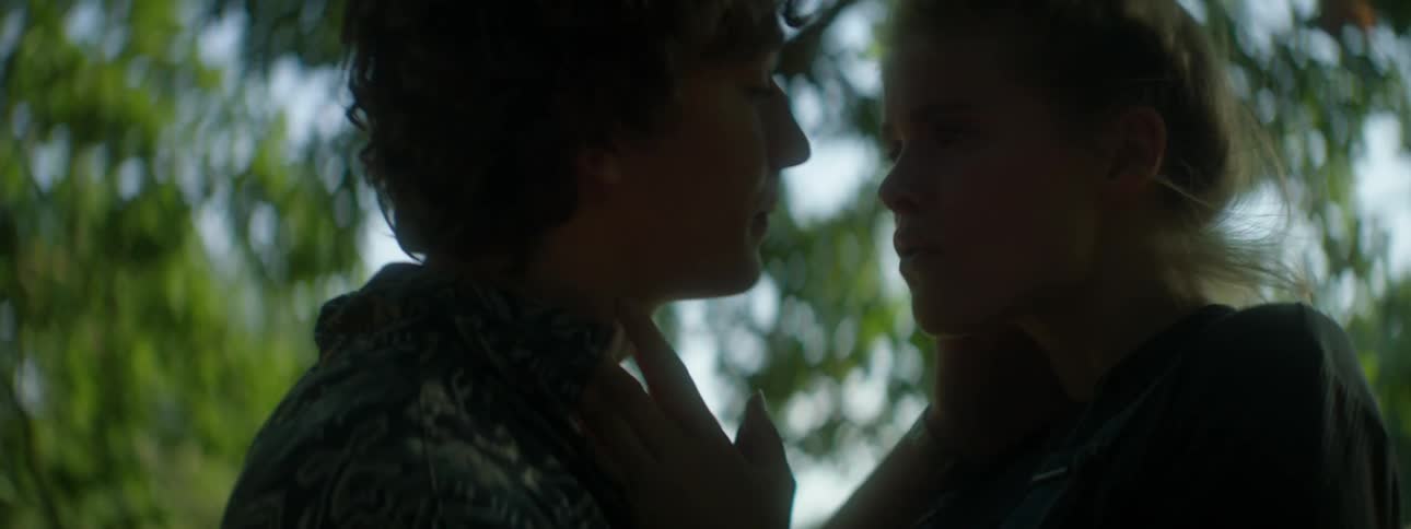 Man and woman kiss and touch each other under a tree