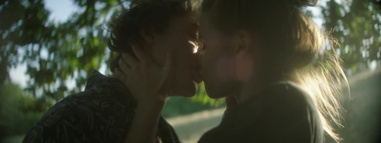 Man and woman kiss and touch each other under a tree