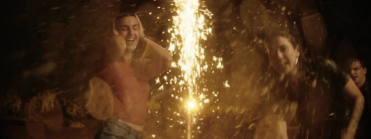 Three friends splash water at one another while flares go off