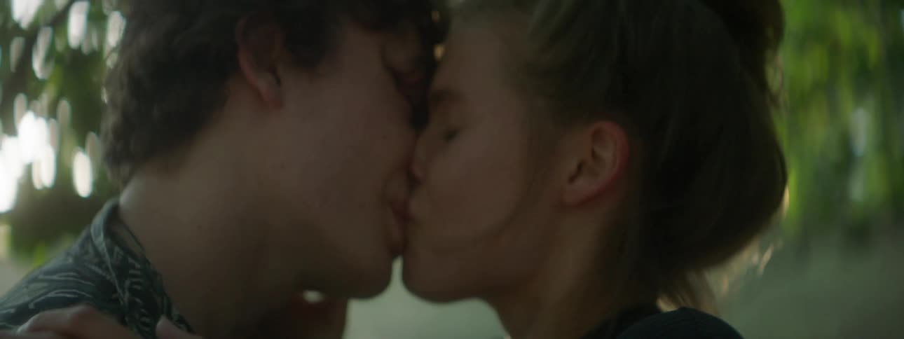 Man and woman kiss and touch each other under a tree