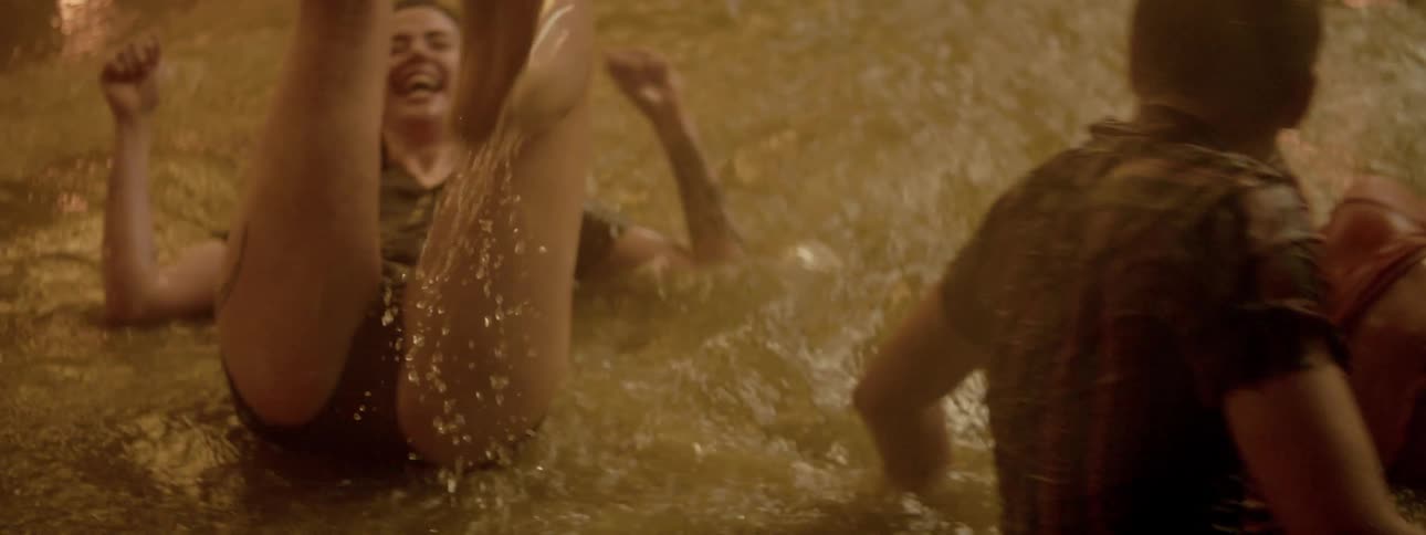 A man and two young women playing in a pool as fireworks on the pools perimeter send colorful sparks into the night air