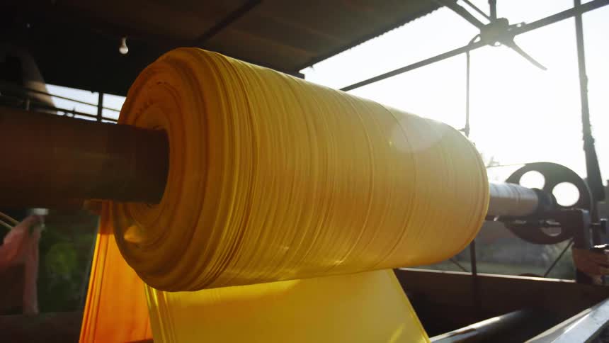 A man sweeps as a machine unravels a big roll of material