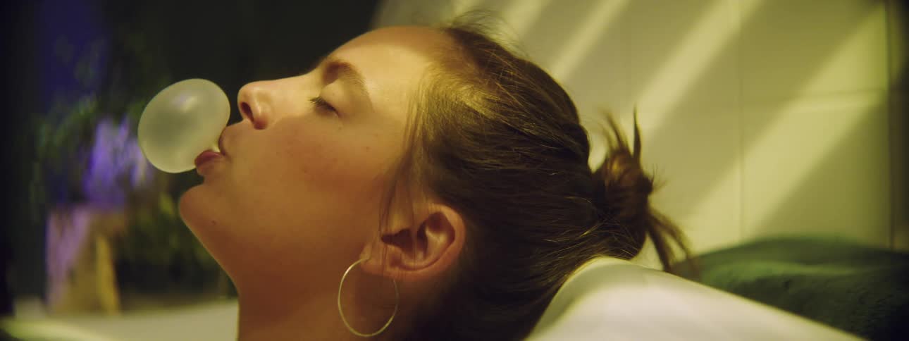 A woman chews gum and blows bubbles while taking a bath