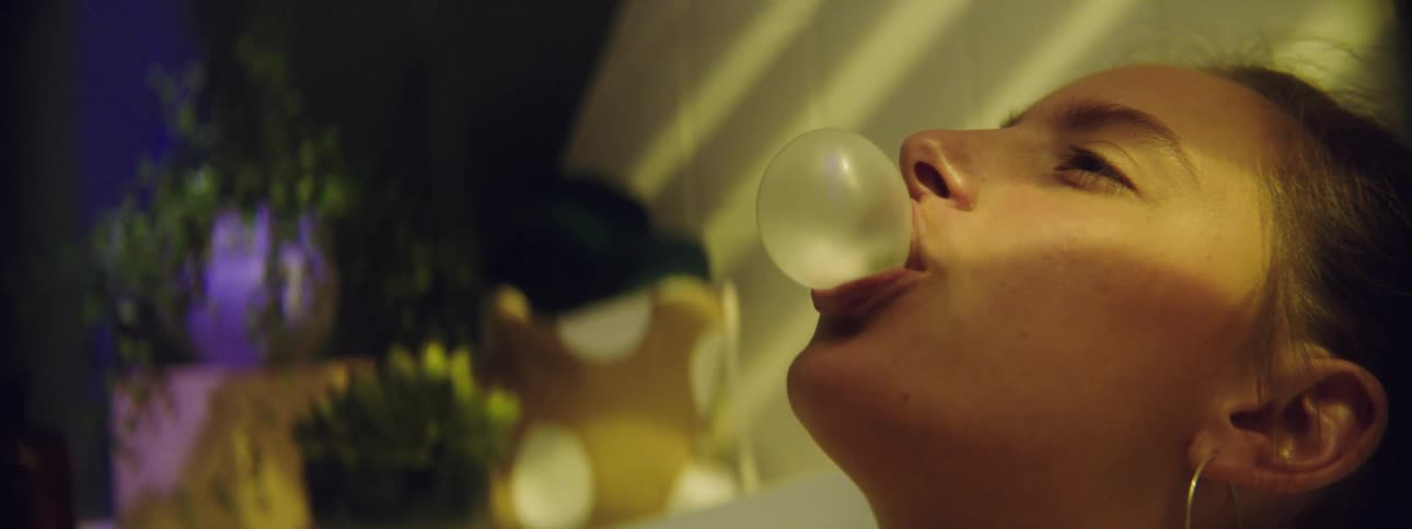 A teenager blows a bubble with her chewing gum and smiles