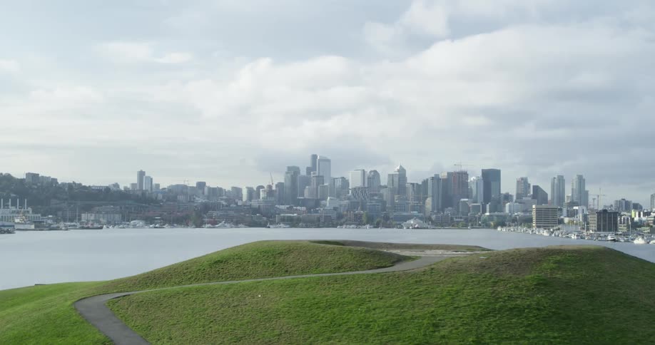 A park with a grassy hill gives way to a view of a large downtown area on a coastline