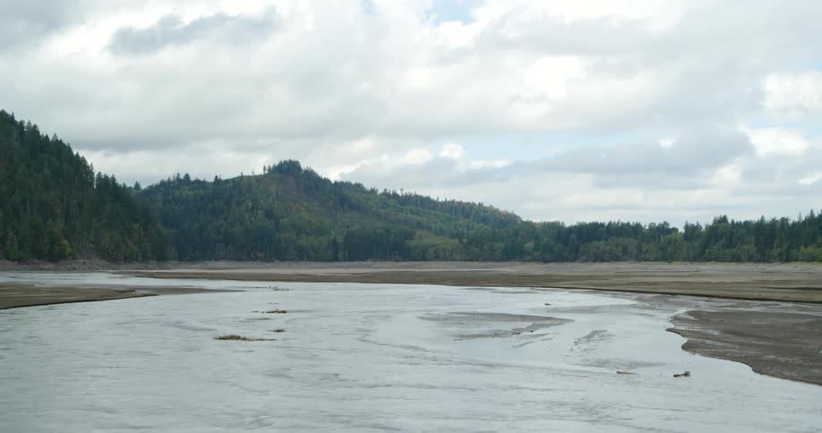 Shallow but wide streams of water flowing across a vast field of soil below forested hills