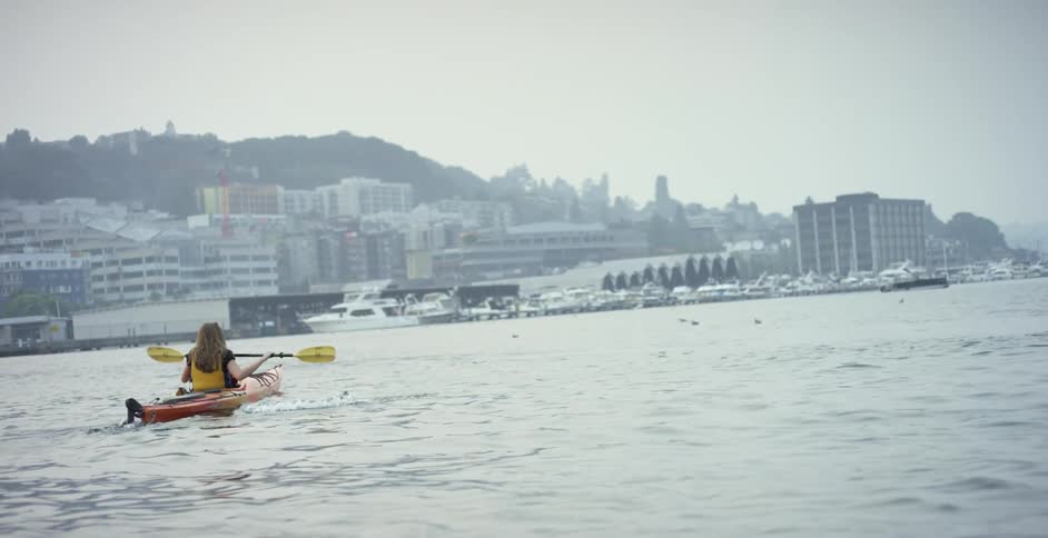 A woman is rowing in the river by the city