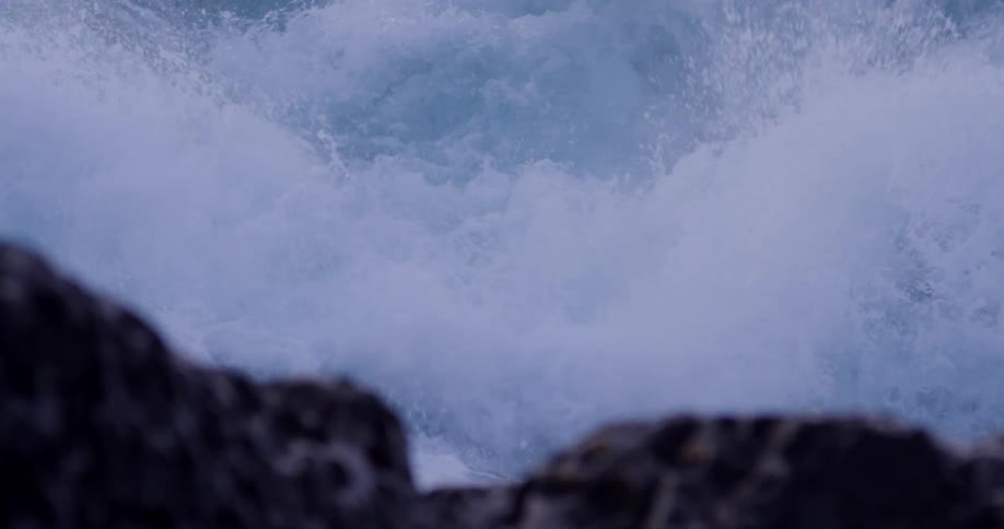 Ocean waves crash over the rocky shore splashing up and creating foam
