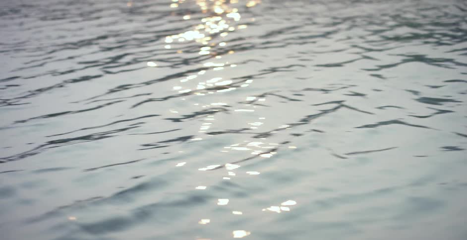 Ripples flow across glossy surface of water reflecting bright light