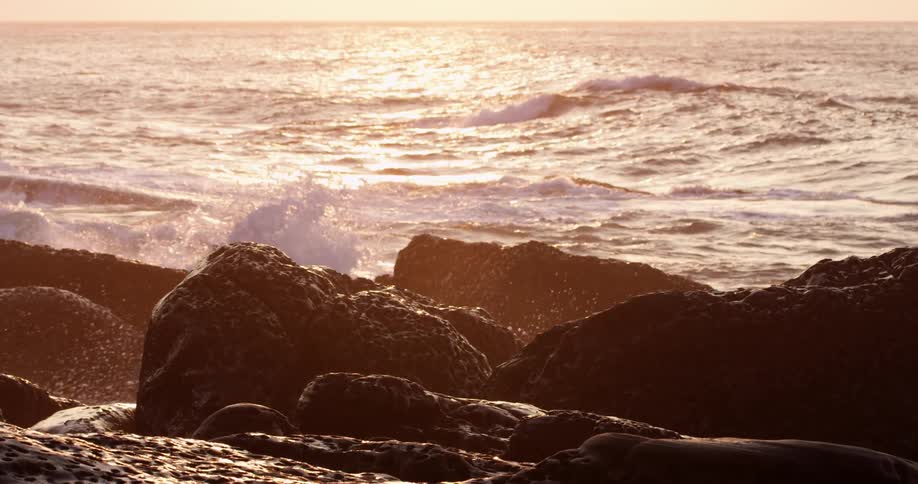 Waves crashing in slow motion on rocks in the coast at sunrise