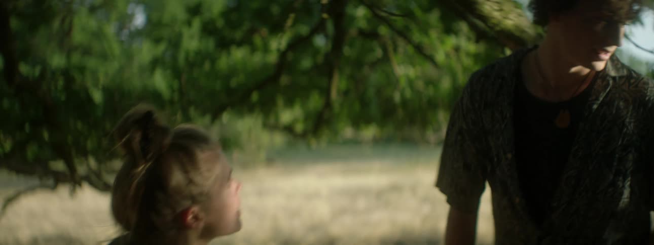 A young woman runs through a rural field pushing angrily at a young man