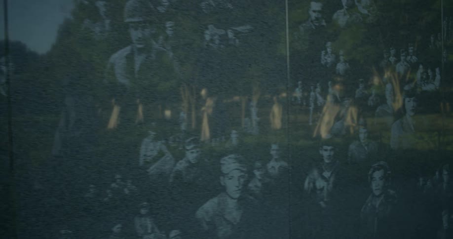 A wall at a war memorial depicts people involved in the conflict while reflecting statues of soldiers in the park
