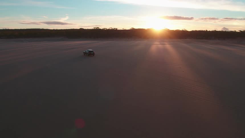 A car drives across the beach as the sun sets
