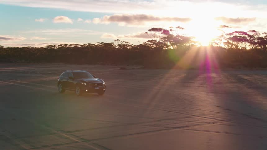 Aerial view of a car driving on sand road at sunset