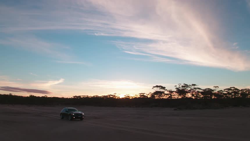 Aerial view of a car driving on the dirt road at dusk