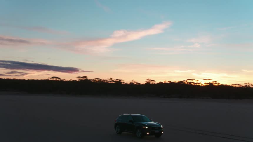 Vehicle drives on the dirt road in the field at dusk