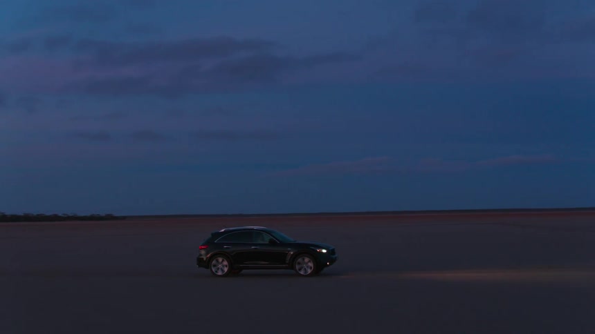 A black sport utility vehicle drives through a barren desert at night