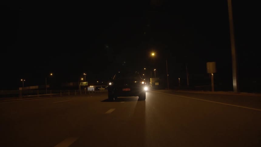 A pair of darkly colored vehicles changing lanes as they travel down a wide road at night