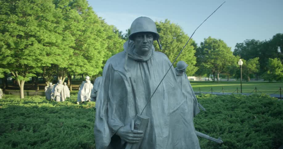 Statues of Korean War soldiers stand in bushes at a monument
