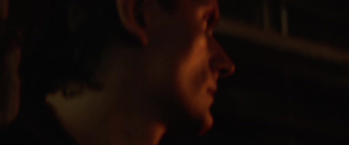 A white man stands in a cramped alley in a neighborhood and looks to a light source
