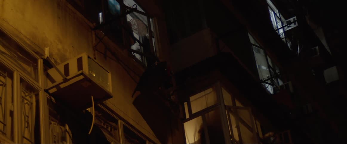 A shirt blowing in the wind while hanging under a window on the facade of a building at night