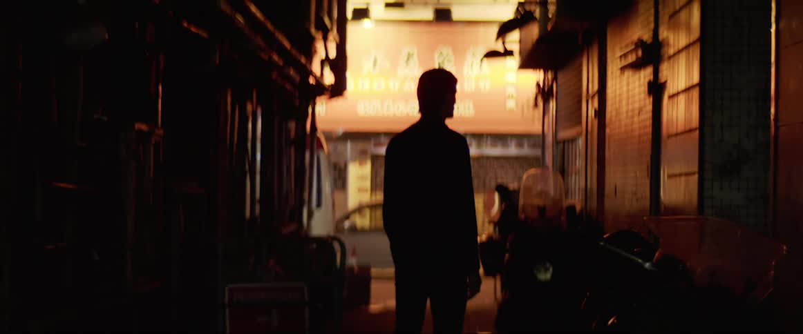A man stands in a dark alley next to motorcycles