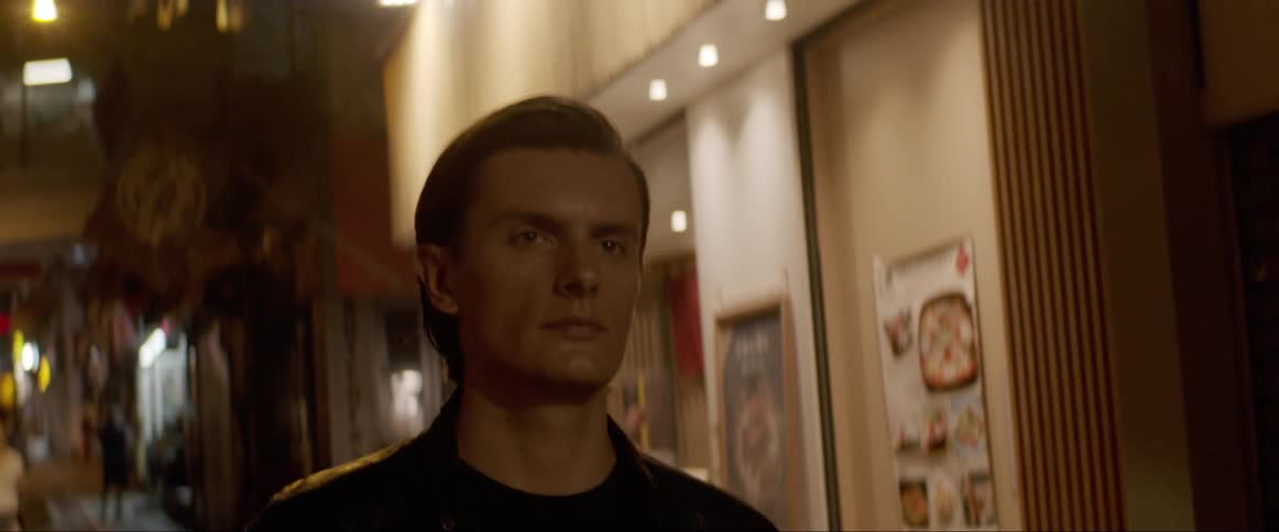 Man wearing a black leather jacket walks down the street at night