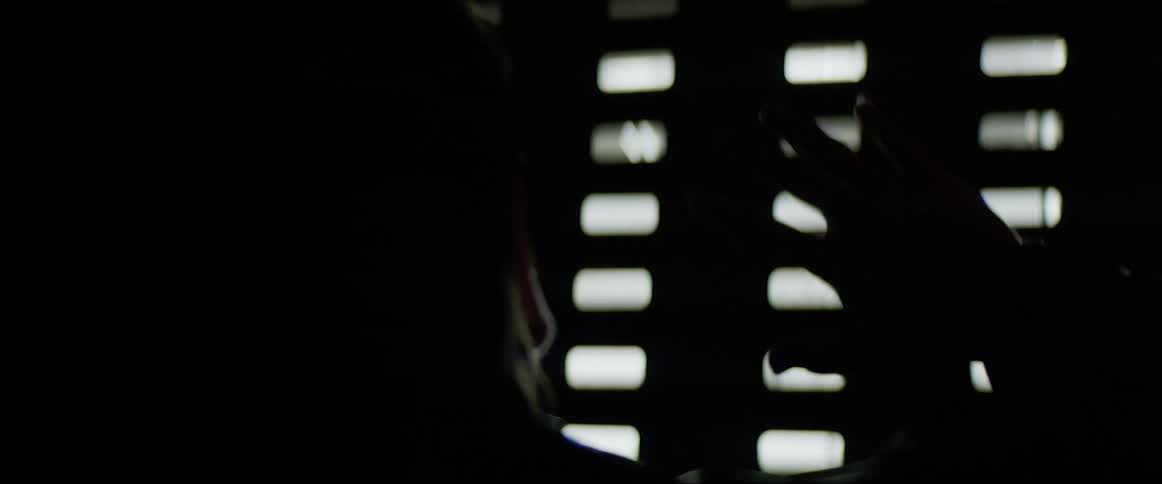 A man holds up his hand to block the glaring light coming in through the grate openings