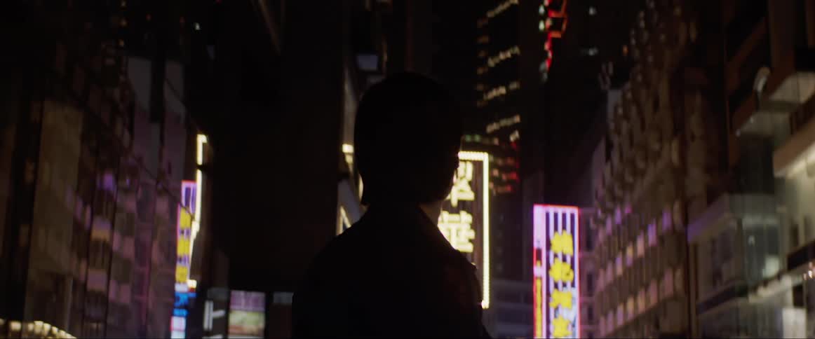 Man walks in a city retail area and looks around at the businesses at night
