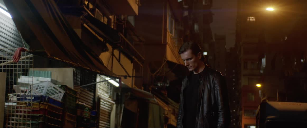 Man in a black leather jacket raises his head as he stands in a lit room