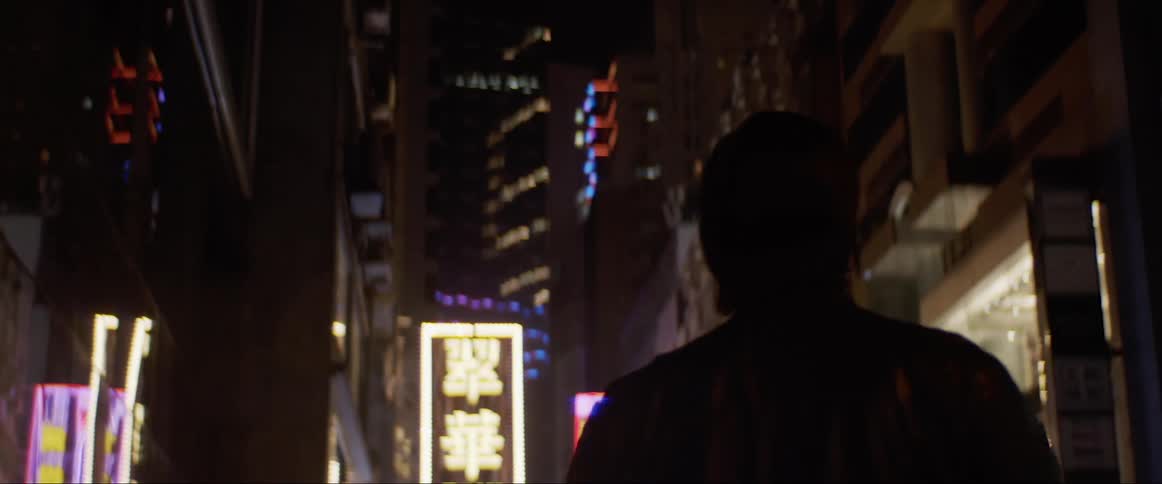 A man walking down a city street at night stops and looks around before walking again
