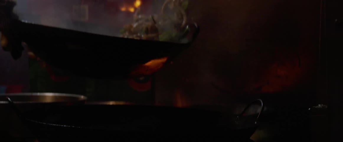 A street cook fries food in a pan that belches flames