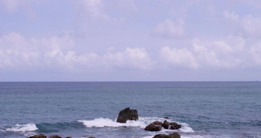Ocean waves crash on the rocks of a coast under a blue cloudy sky
