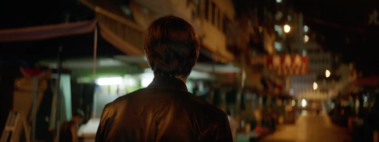 Man wearing a leather jacket walks down the street at night