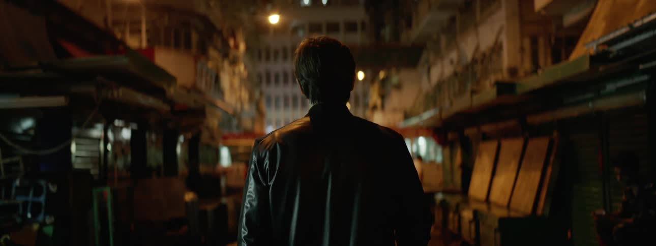 Man wearing a leather jacket walks down the street at night