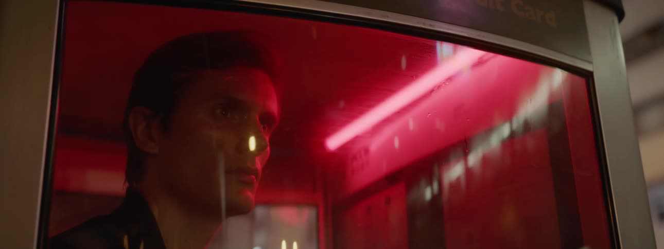 A white man stands in a glass booth and looks out a window