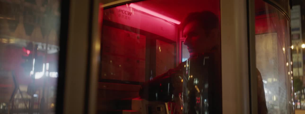 A white man stands in a phone booth bathed in red light in the downtown area of Hong Kong city