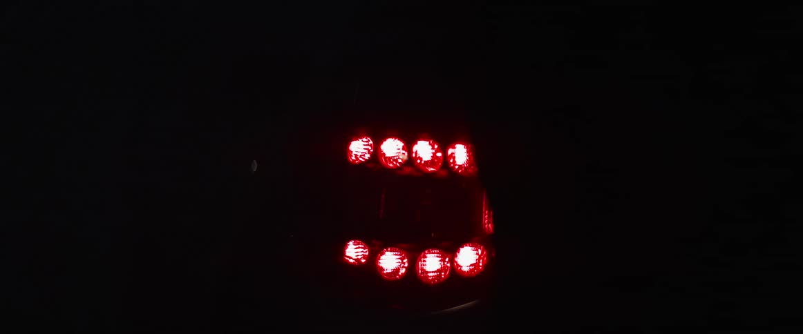 A white woman walks past a cars lit up tail light and rubs the vehicle with her hand