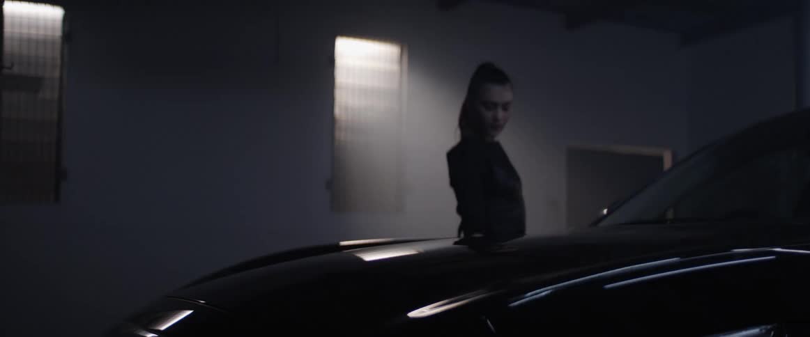 Woman walks around a car in a dimly lit garage