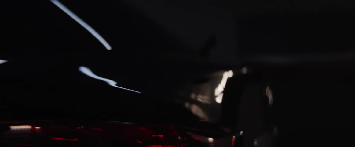 Woman walks around a black car on a dimly lit room with strobing lights