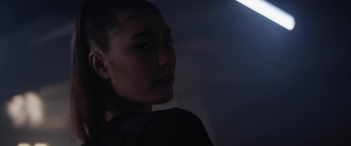 An asian woman stands in a building with flickering lights and looks around