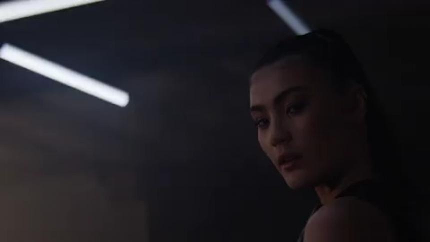 Woman with pony tail turns to look over shoulder under flickering fluorescent lights