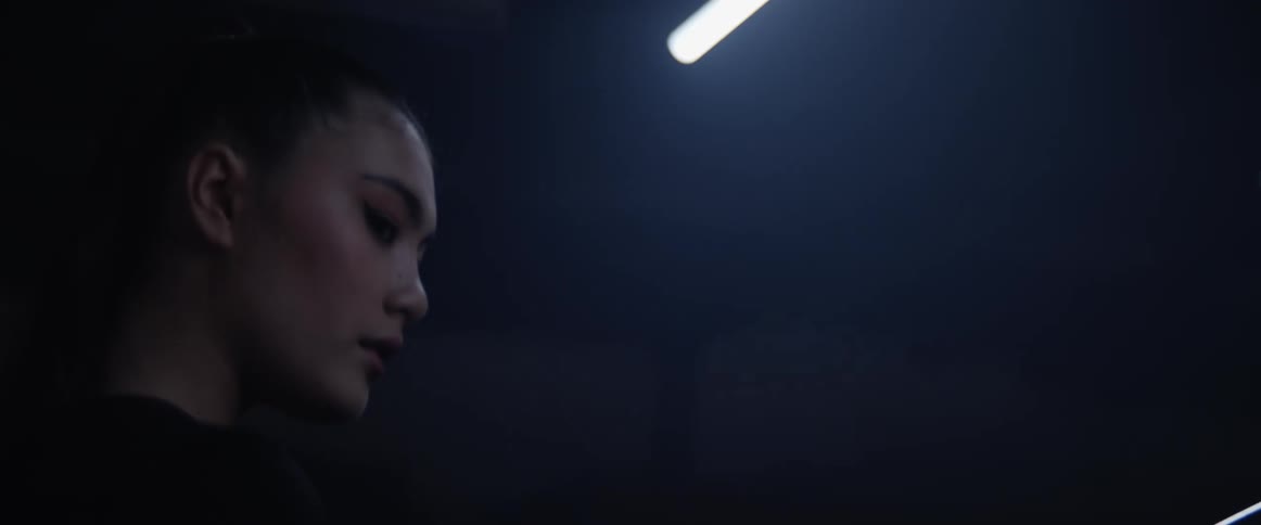 A woman stands in a dark room with the light flickering