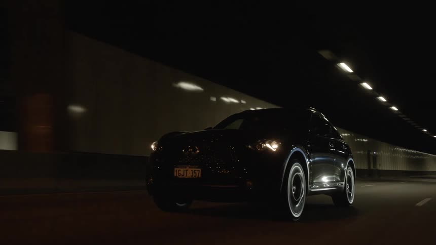 A black sport utility vehicle drives through a tunnel that exits into a city neighborhood