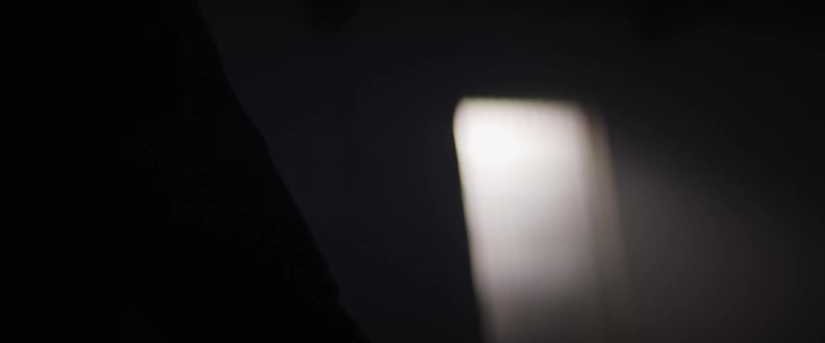 Woman strokes car hood in dark room lit by light shining through door